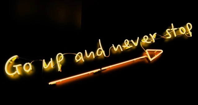 A neon sign with words 'Go up and never stop'